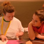 During craft time at Champions Camp, a participant diligently completes her task at hand while her buddy looks on in amazement.
