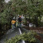 Illinois Baptist Wayne Laechelt (right) used a pole saw to cut limbs that were hanging precariously over a Mandeville homeowner’s roof as Ken Cummins holds out a hand to steady him. TAB Media photo