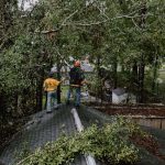 Illinois Baptist Wayne Laechelt (right) used a pole saw to cut limbs that were hanging precariously over a Mandeville homeowner’s roof as Ken Cummins holds out a hand to steady him. TAB Media photo